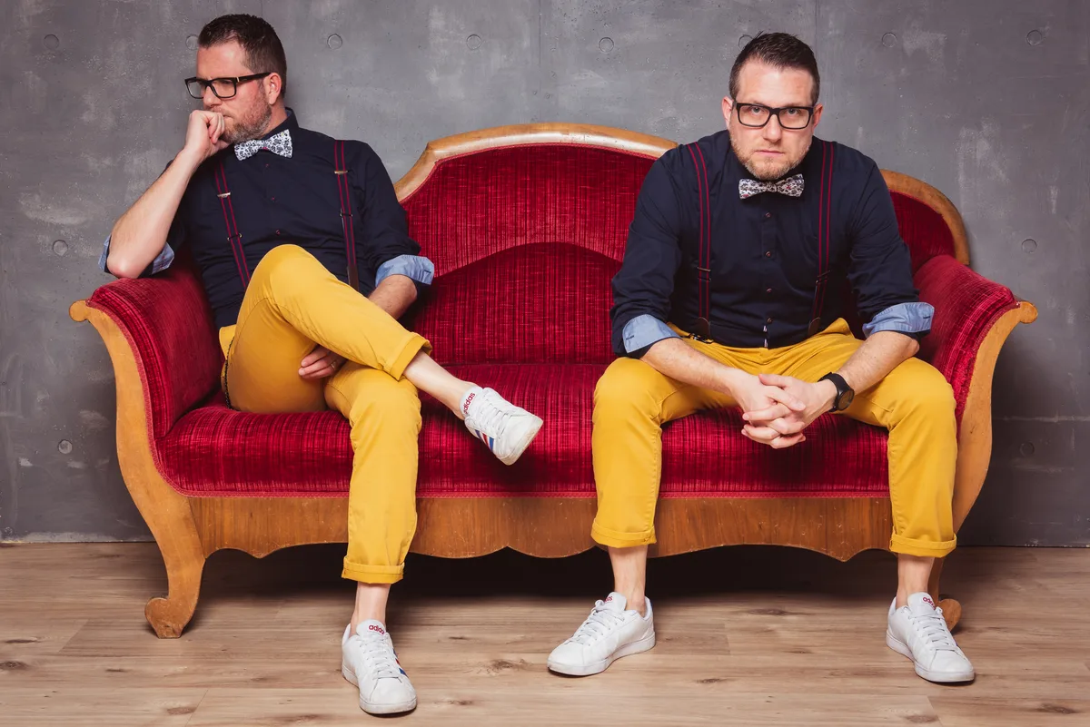 Roland und Matthias Portmann sitzen in gleichen Kleidern auf einem Sofa.